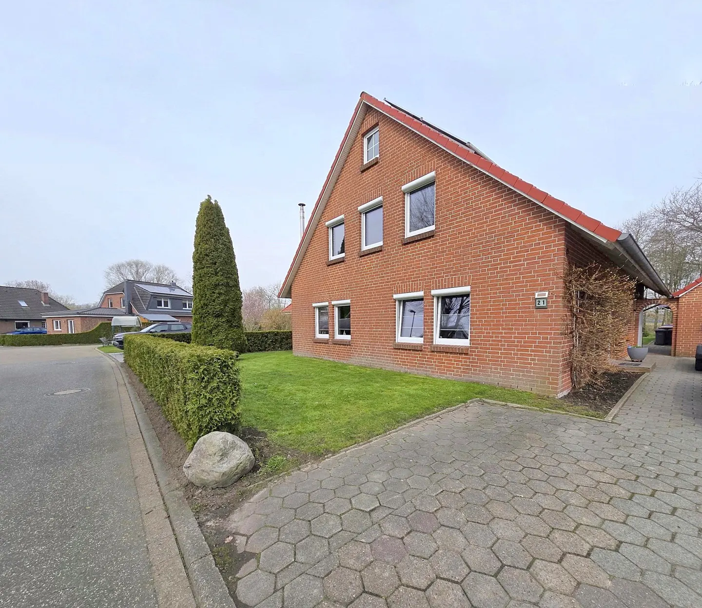 Red brick house with white framed windows, green lawn, and a gray stone driveway.