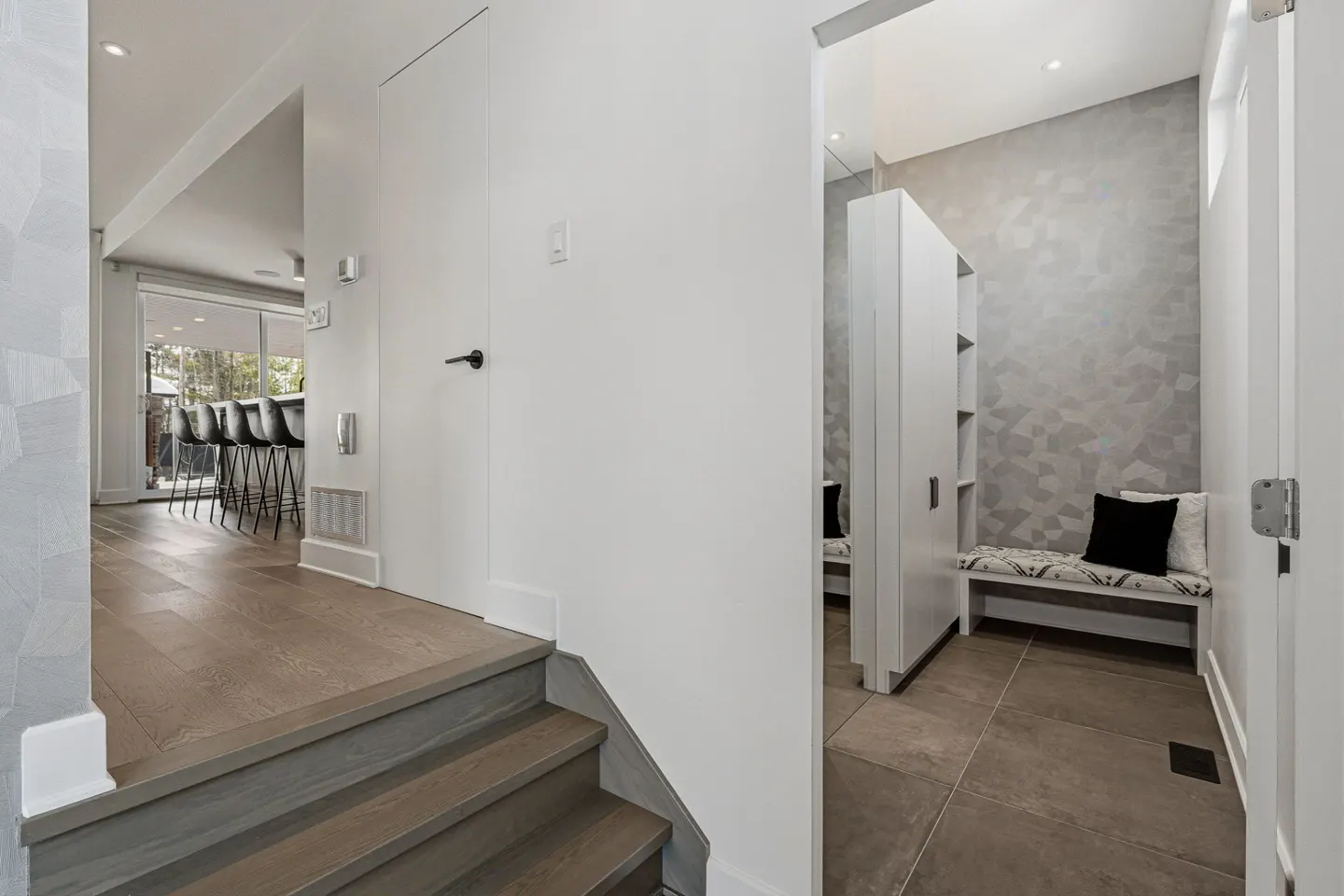 Interior view of a modern home with hardwood floors, white walls, and a bench with pillows in a hallway.