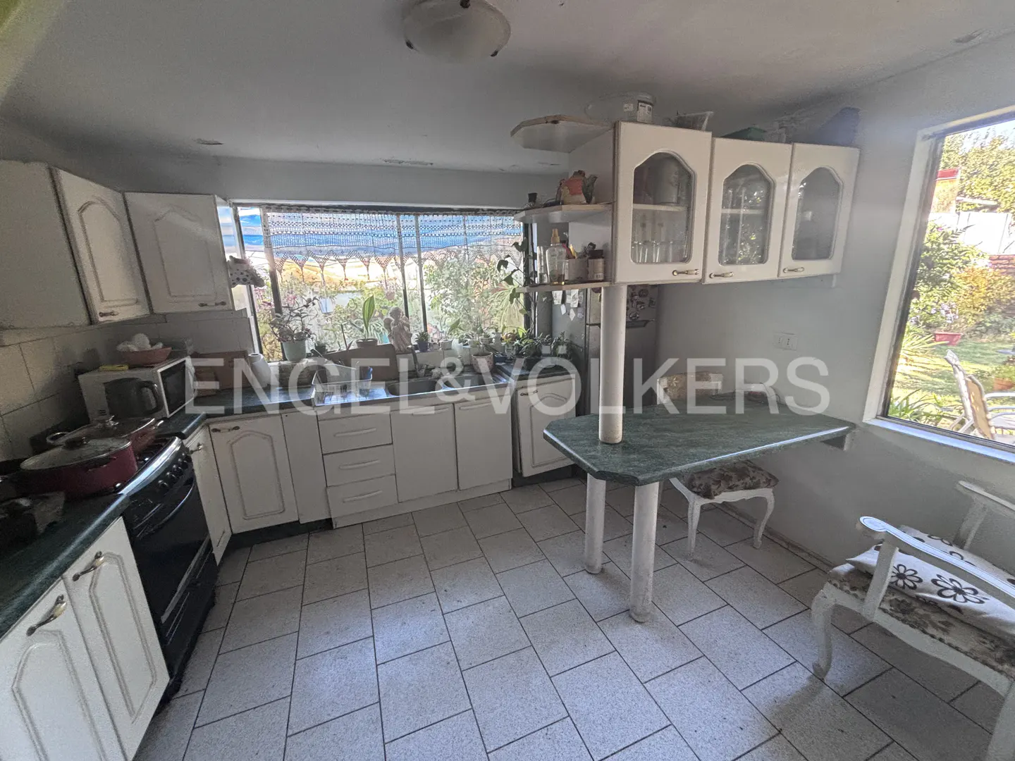 A bright kitchen with white cabinets, a green countertop table, and a window overlooking a garden.