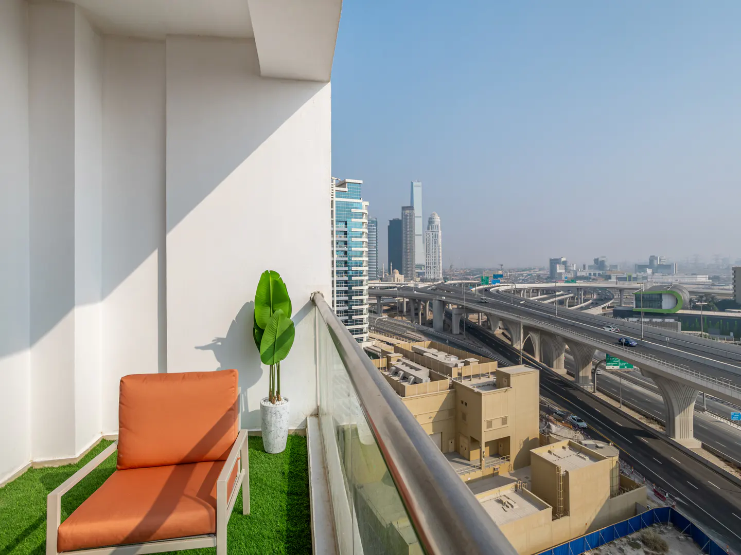 Balcony view with orange chair, potted plant, and city skyline. Highway overpasses are visible in the background.