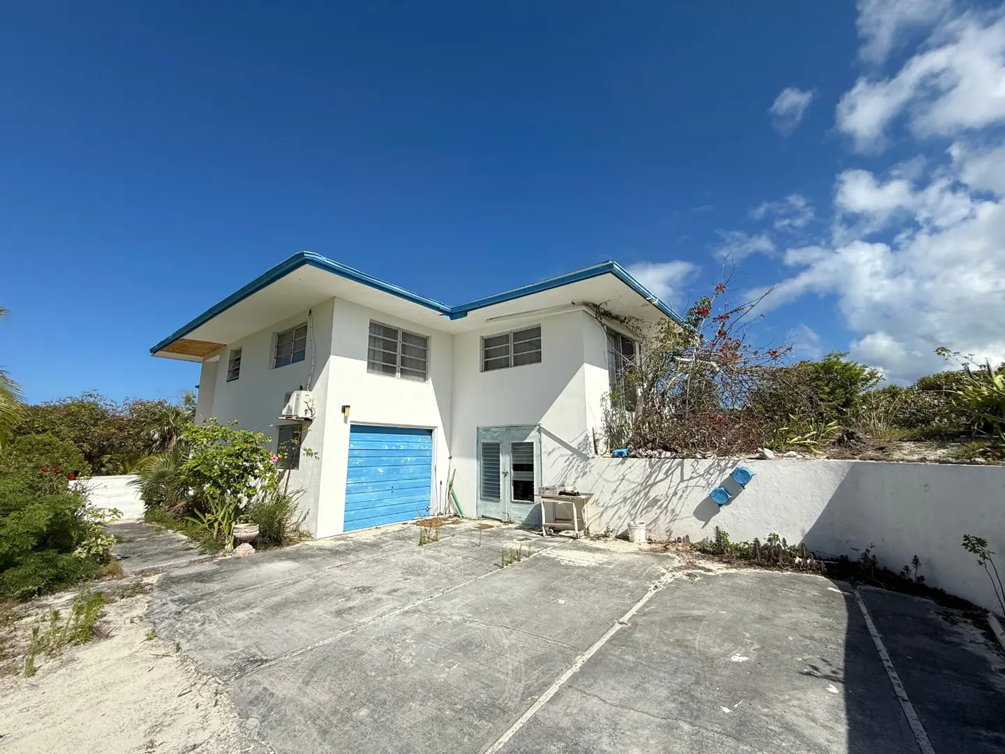 Two-story white house with a blue garage door and trim under a bright blue sky with scattered clouds.