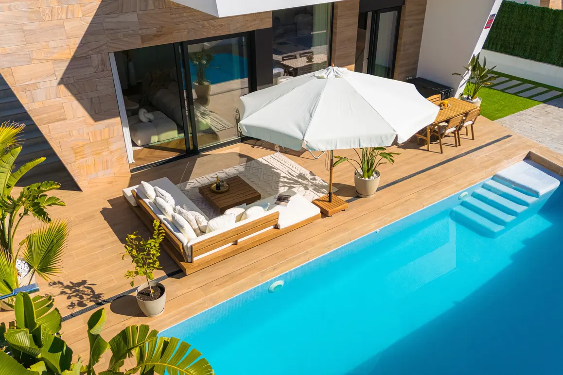Aerial view of a modern home's outdoor space with a pool, lounge seating, dining table, and white umbrella.