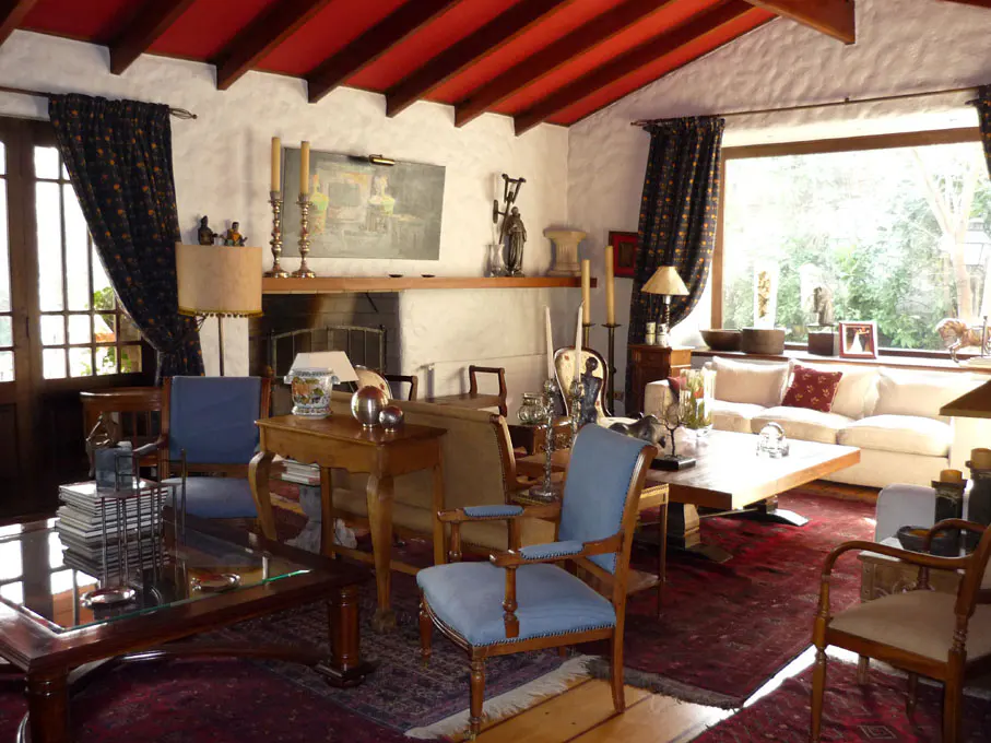 Living room with red ceiling, white walls, and dark curtains. Furniture includes blue chairs, wooden tables, and a white sofa.