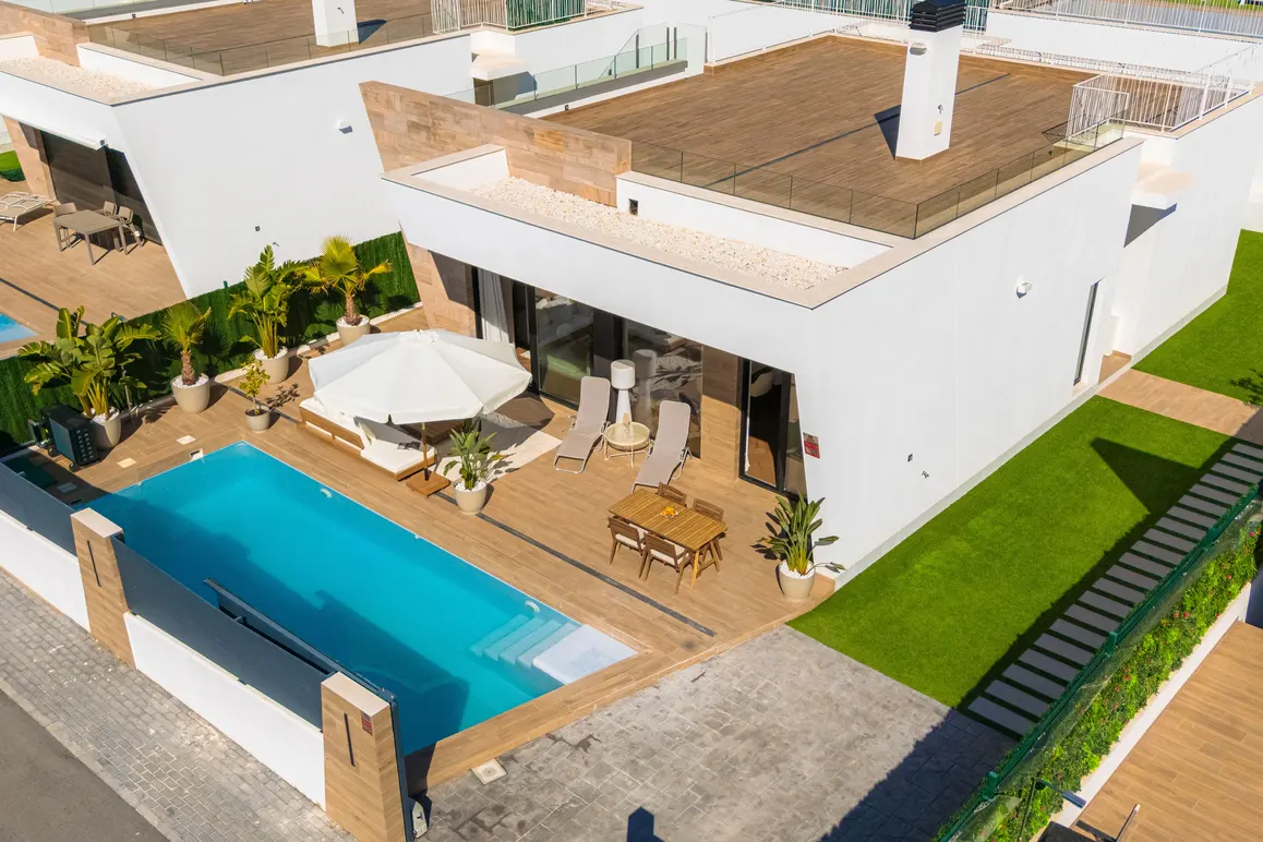 Aerial view of a modern white house with a pool, patio furniture, and green lawn.