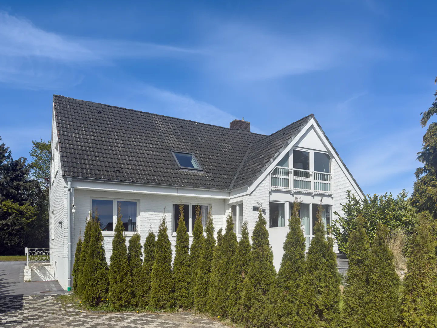 A white, two-story house with a dark gray roof and green trees in front of it.