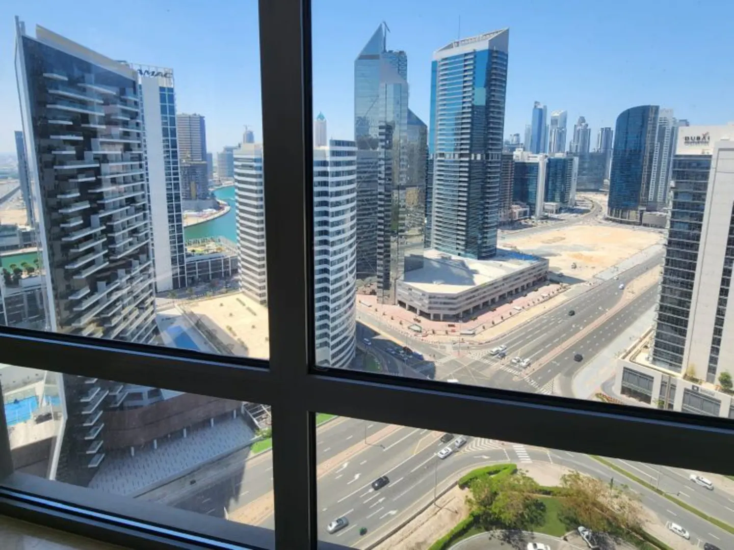 View from a window of a city skyline with tall buildings, roads, and cars on a sunny day.