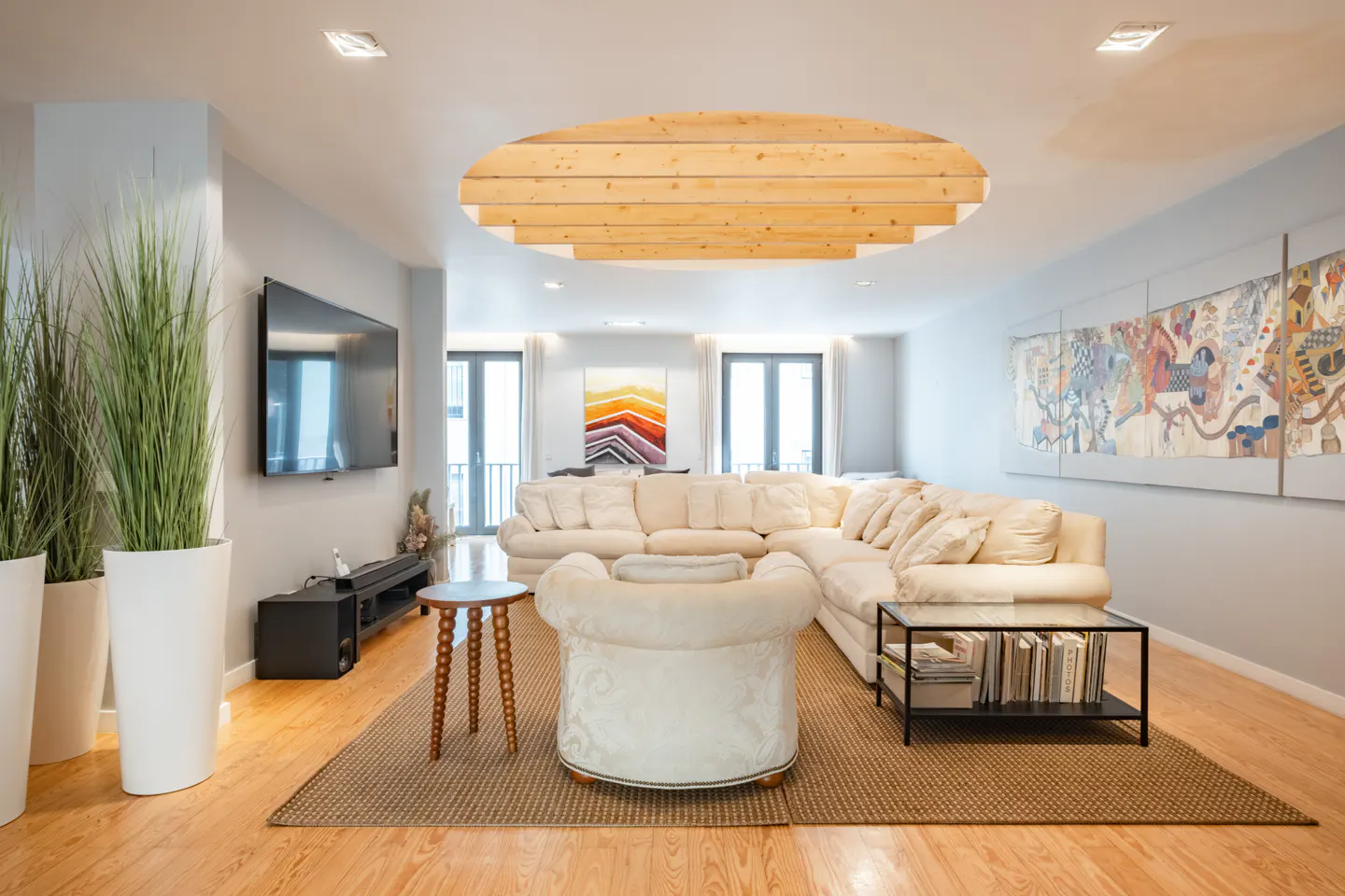 Bright living room with a large white sectional sofa, wood floors, and a decorative wood ceiling feature. A large tapestry hangs on the wall.