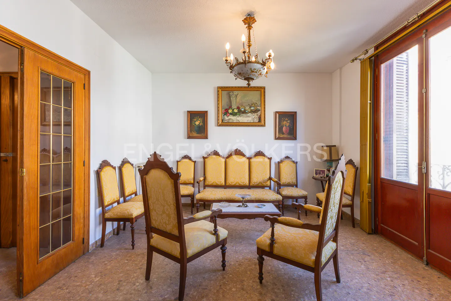 A living room with yellow upholstered chairs and sofa, a chandelier, and framed art on the white walls.