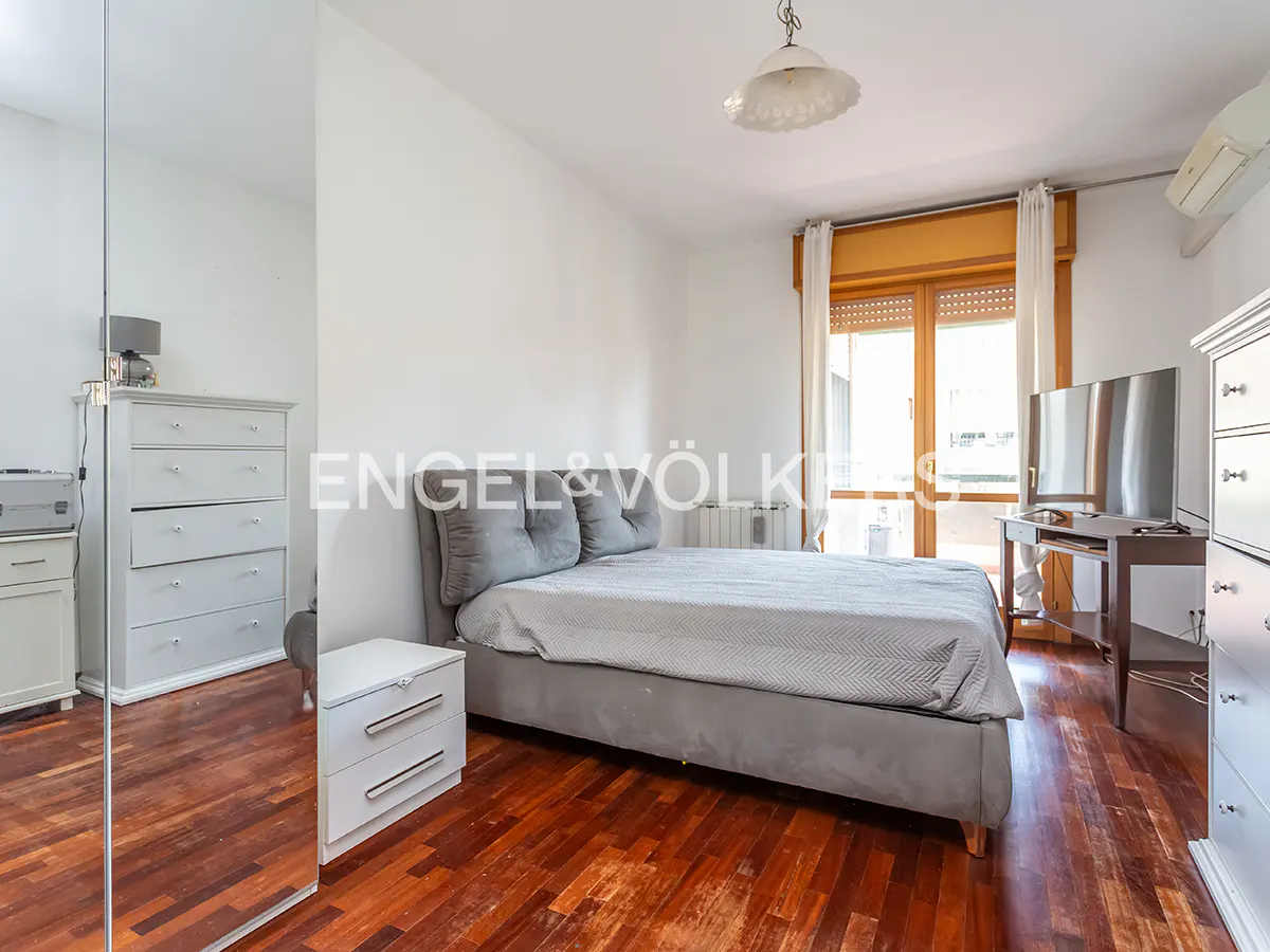 Bedroom with gray bed, wood floors, white walls, and a mirrored closet. A TV sits on a table near a window.