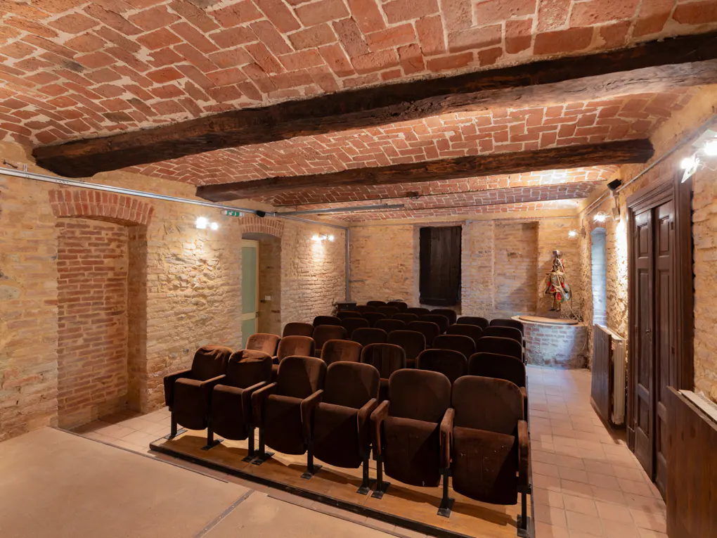 Interior view of a small theater with brown velvet seats, brick walls, and a brick ceiling with dark wood beams.