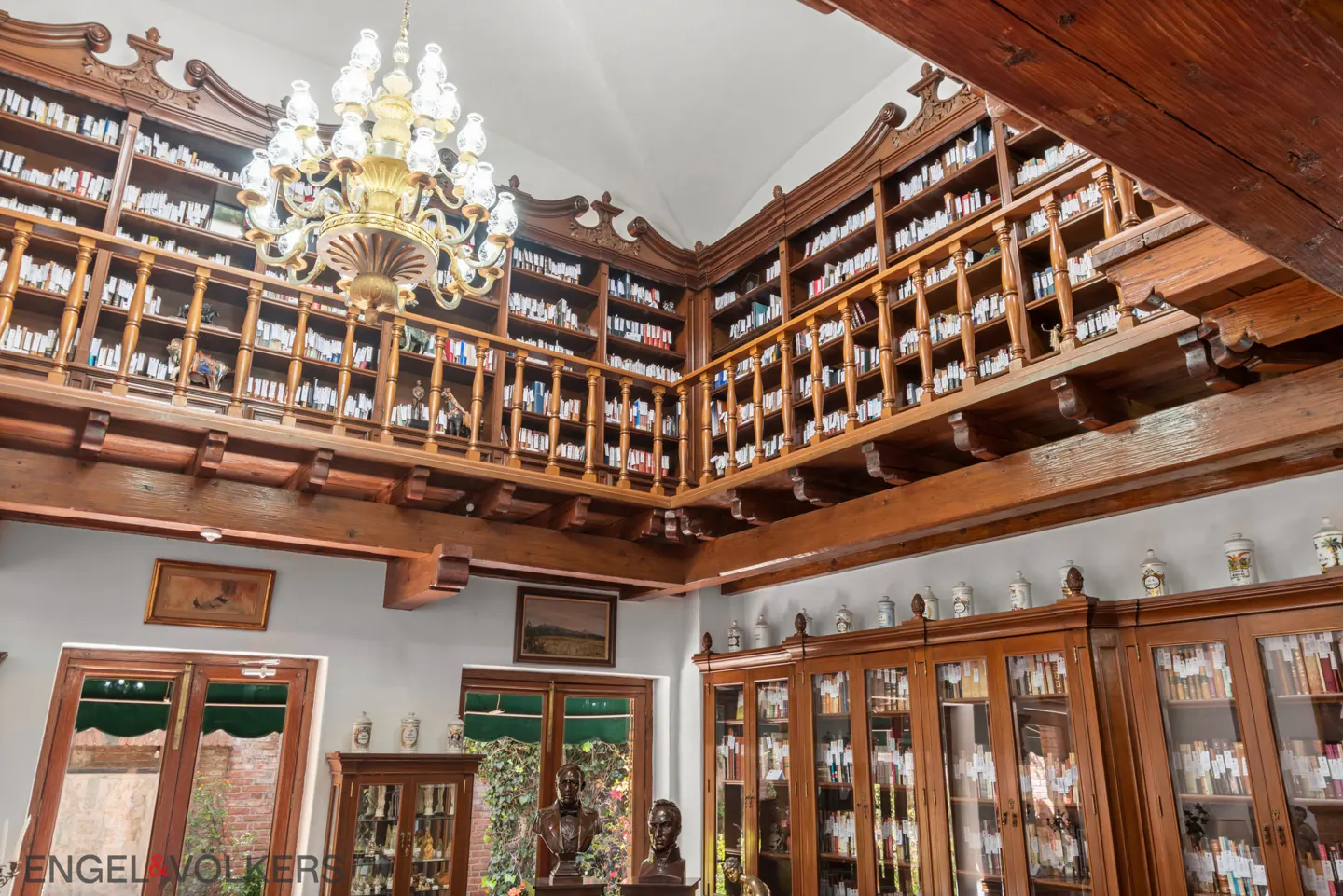 A room with floor-to-ceiling wooden bookshelves, a chandelier, and busts.