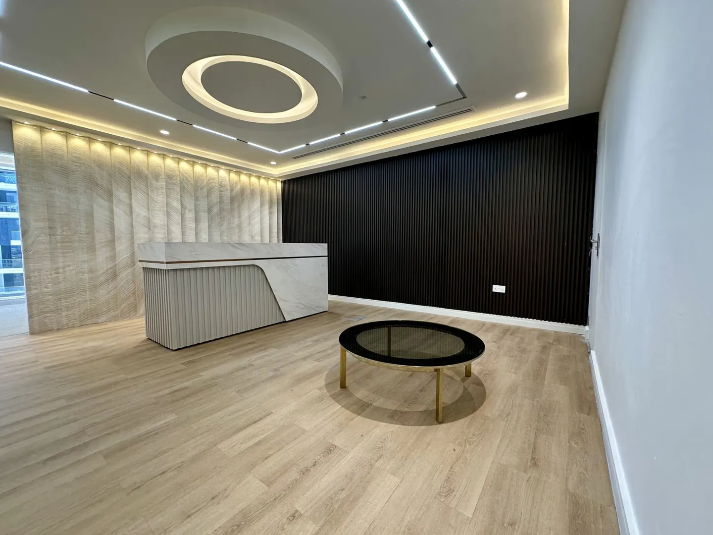 Modern office space with a reception desk, black accent wall, and round coffee table on a light wood floor.