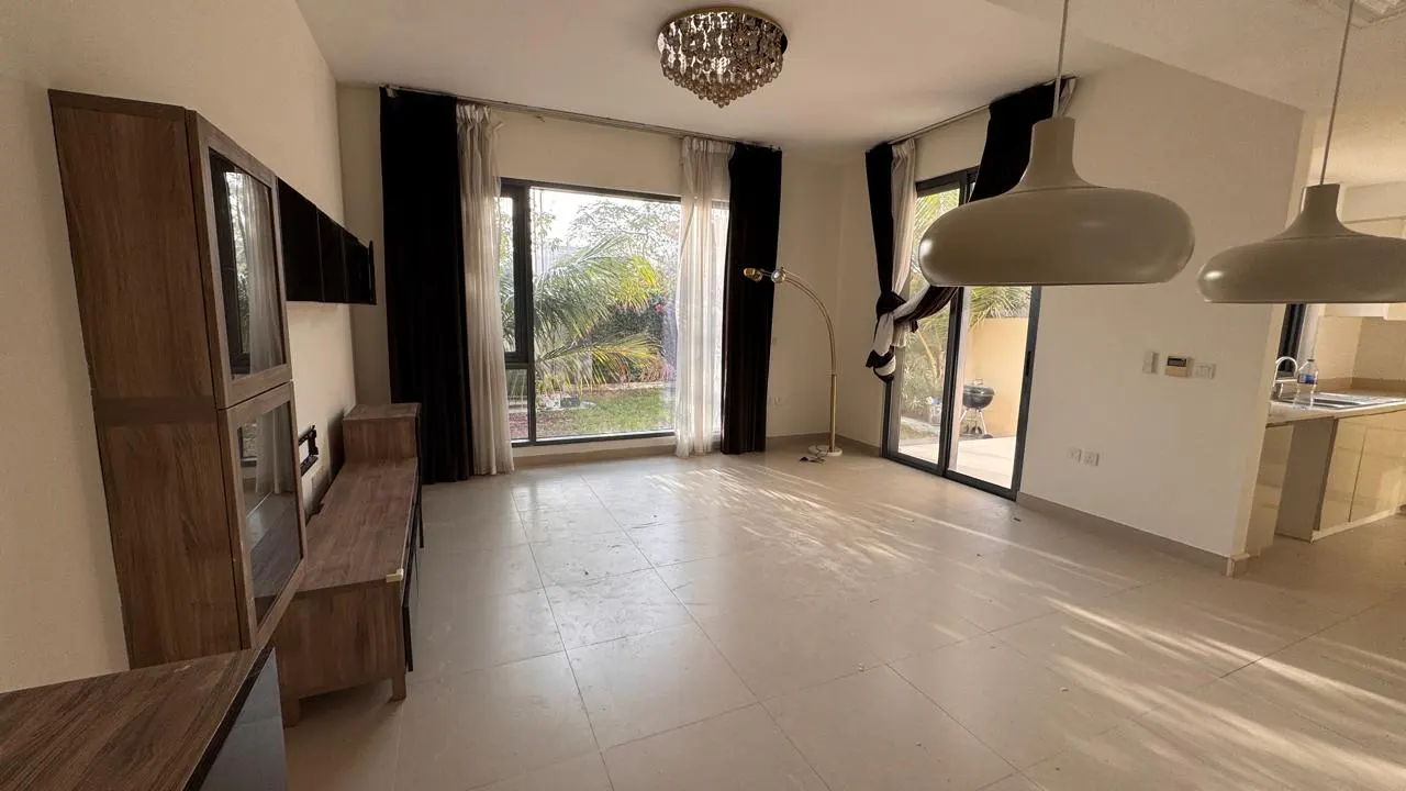 Bright living room with tile floors, wood entertainment center, and large windows with black curtains overlooking a green yard.