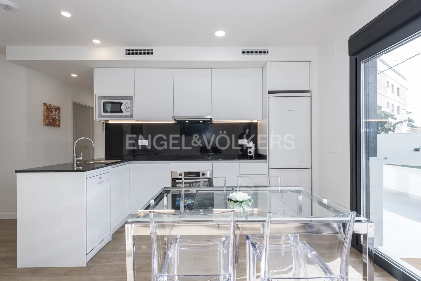 Bright kitchen with white cabinets, black backsplash, and stainless steel appliances. A clear table and chairs sit in the foreground.
