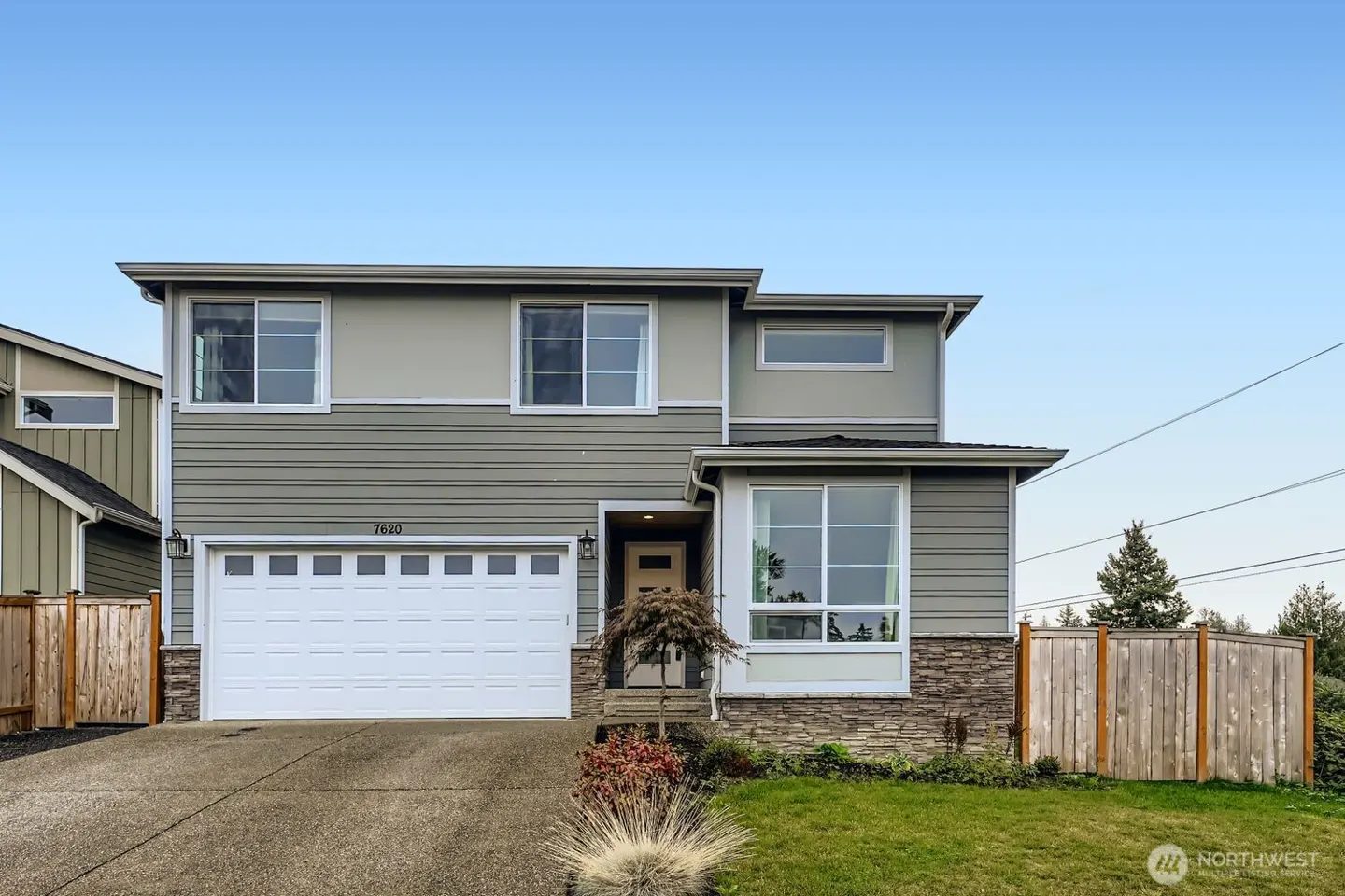 Two-story suburban home with gray horizontal siding, stone accents, a white two-car garage, and a concrete driveway.