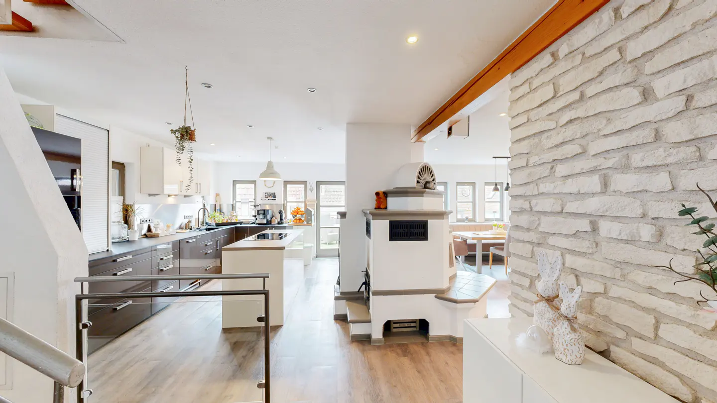 Bright, open-concept kitchen with wood floors, white brick wall, and a white stove. A kitchen island and dining area are visible.
