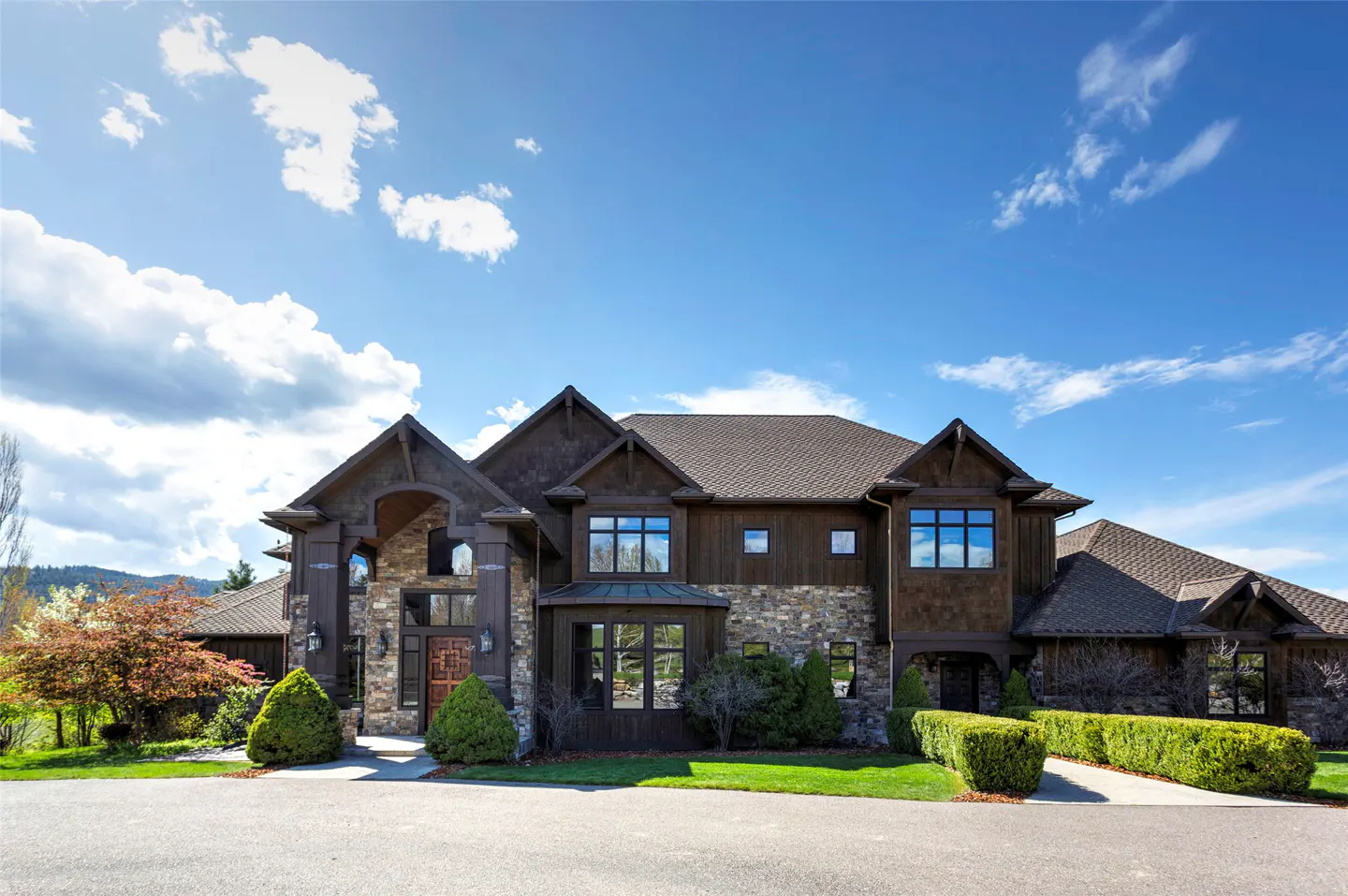 A large, two-story house with a stone and wood facade under a blue sky with white clouds.