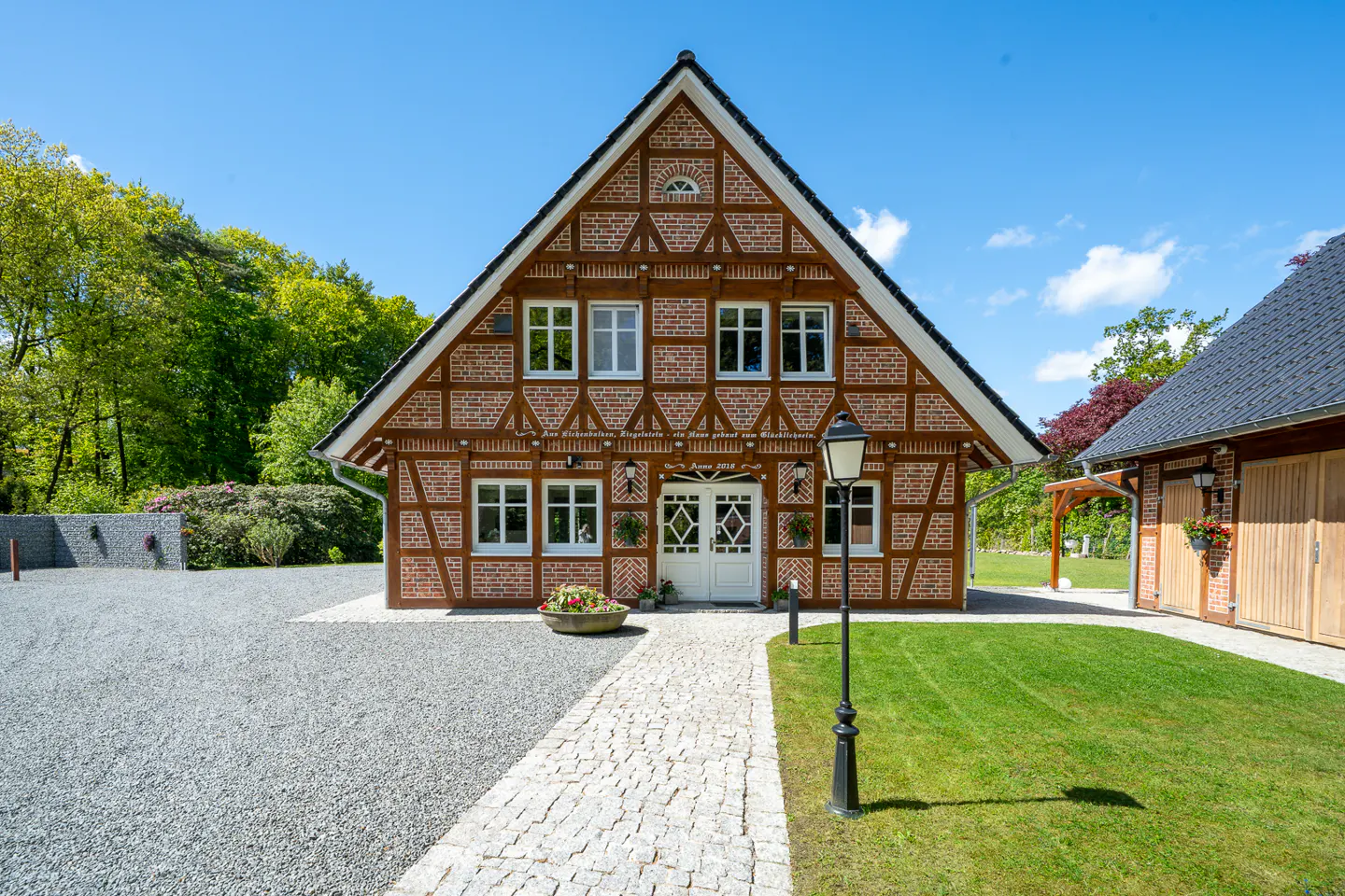 Traditional half-timbered brick house with a stone path, gravel driveway, and green lawn under a clear blue sky.