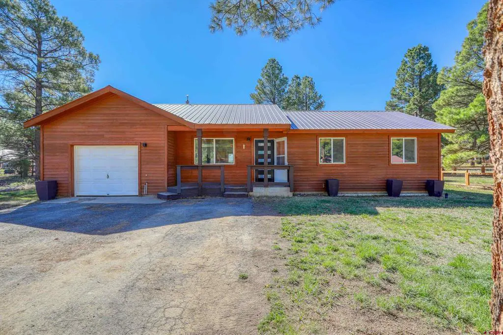 A single-story, wood-sided house with a metal roof, a white garage door, and a lawn.