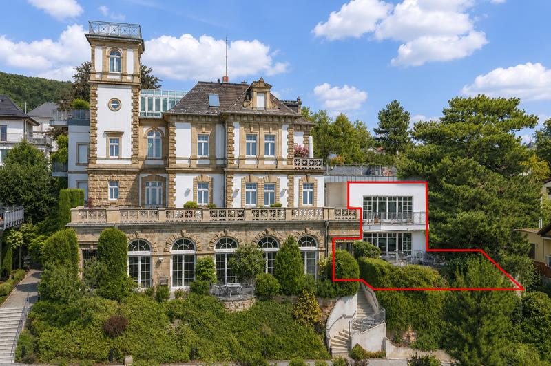 Grand historic villa with a stone facade, tower, and a modern white extension outlined in red, set in a lush garden.