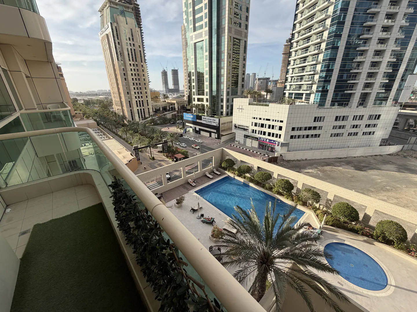 View from a balcony overlooking a blue swimming pool, palm trees, and city buildings in the background.