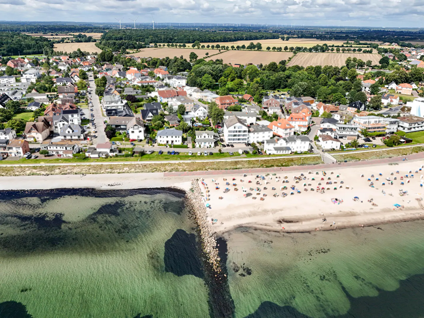 Aerial view of a coastal town with a sandy beach, clear water, and houses with red and gray roofs.