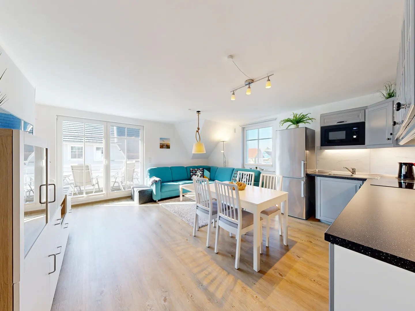 Bright, open-plan living space with a turquoise sofa, white dining table and chairs, and a modern kitchen with gray cabinets.