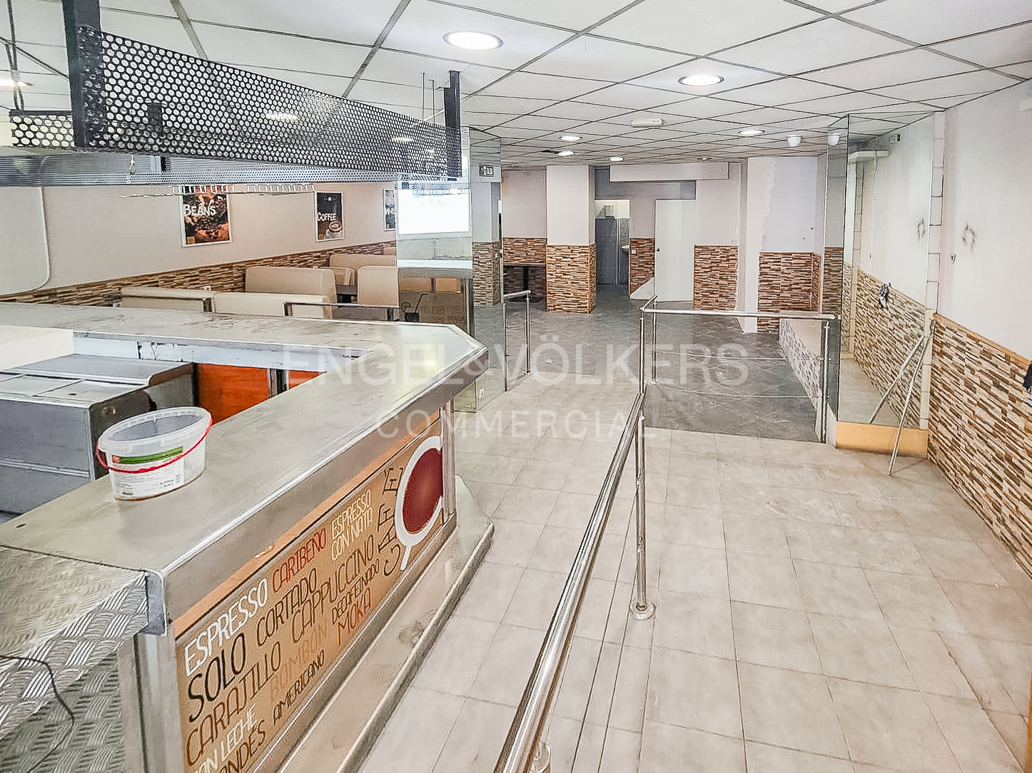 Interior of a cafe with a metal service counter, tiled floors, and walls decorated with stone-look panels.