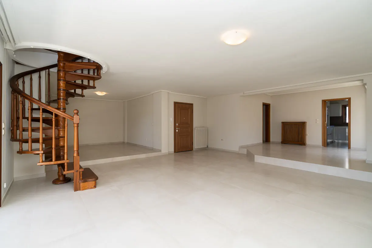 Spacious room with white floors, a wooden spiral staircase, and raised platforms leading to doorways.