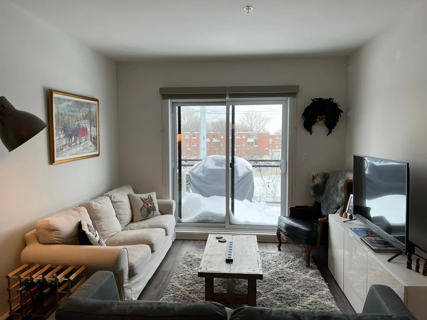 Living room with a beige sofa, wood coffee table, and a sliding glass door to a snowy balcony. A painting hangs above the sofa.