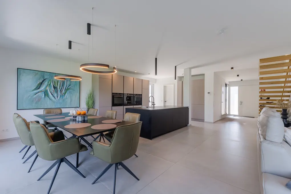 Modern open-plan kitchen and dining area with olive green chairs, a black island, and abstract art on a white wall.