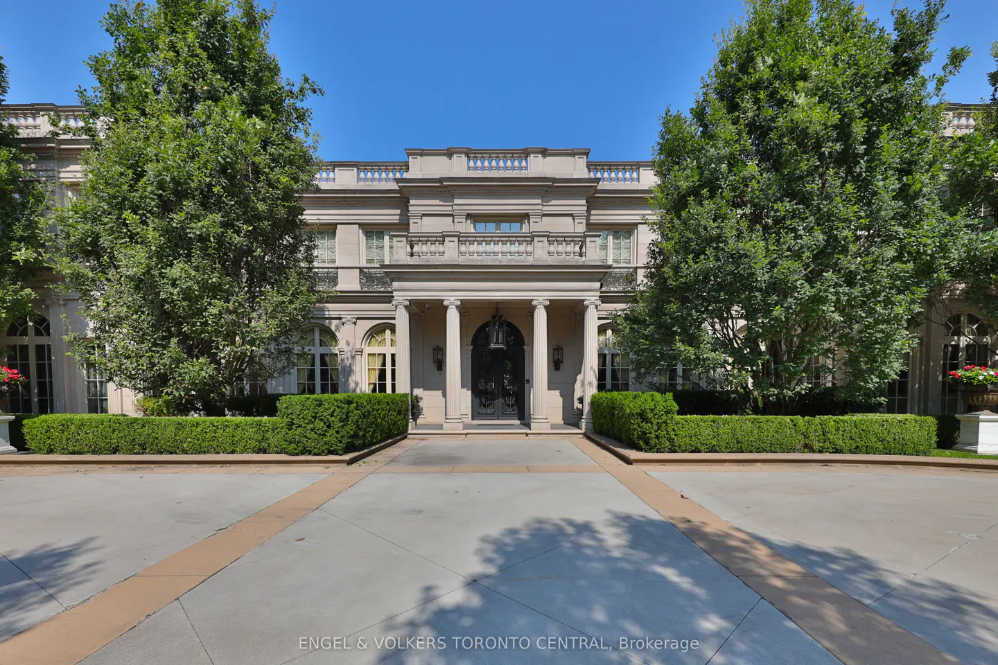 Beige mansion with black double doors, white columns, and green trees on a sunny day.