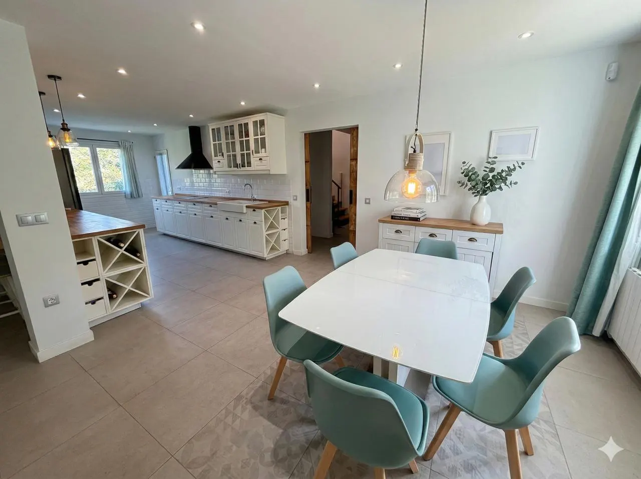 Bright, open-concept kitchen and dining area with white cabinets, a white table, and teal chairs. A modern pendant light hangs above the table.