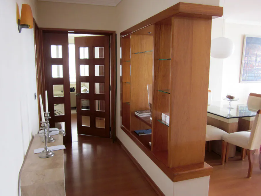 Interior view of a home featuring a wooden room divider with glass shelves, a doorway with a grid pattern, and a dining area.