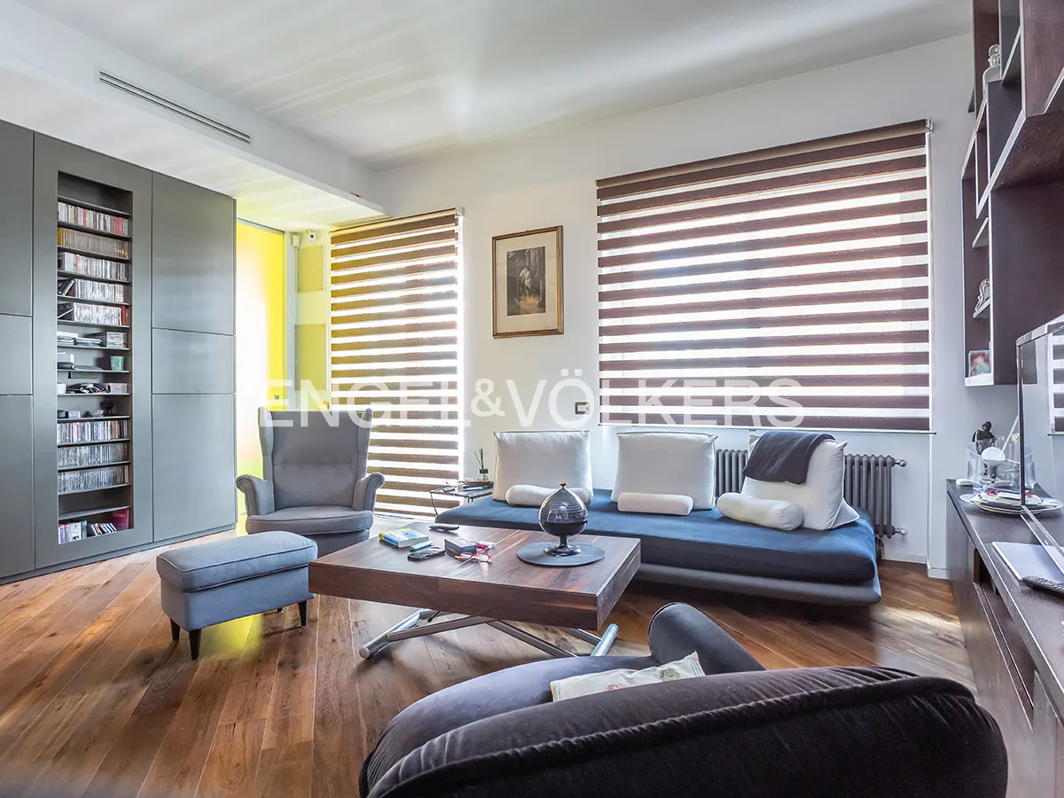 A living room with hardwood floors, a gray sofa, a gray armchair, and a wooden coffee table. Blinds cover the windows.