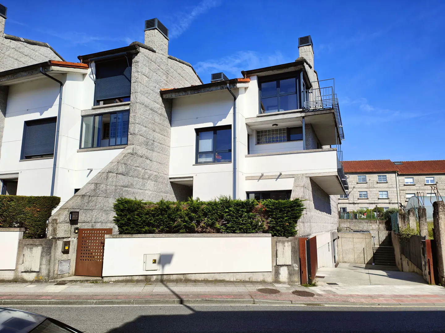 Exterior view of modern townhouses with white walls and gray stone accents under a bright blue sky.
