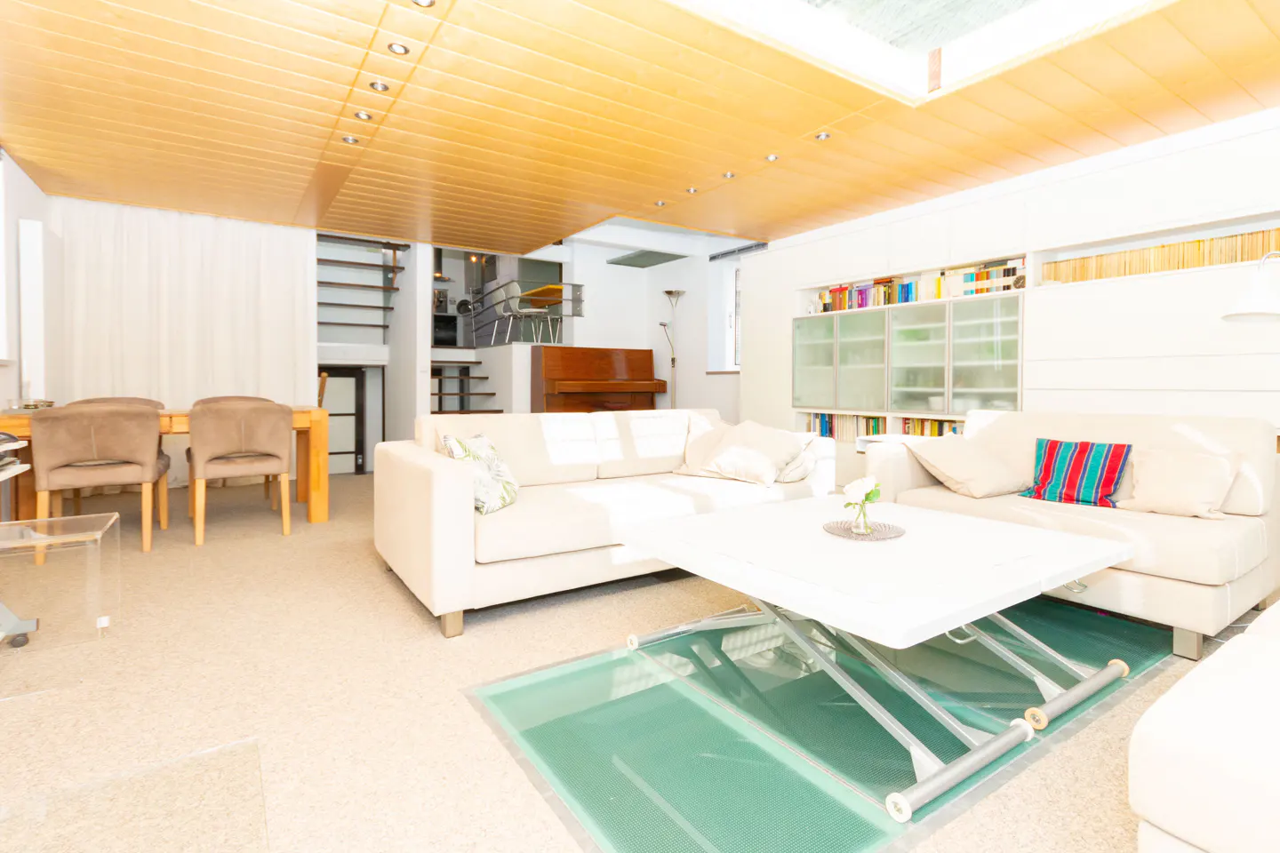 Bright living room with a wood ceiling, white sofas, a glass floor panel, and a piano in the background.
