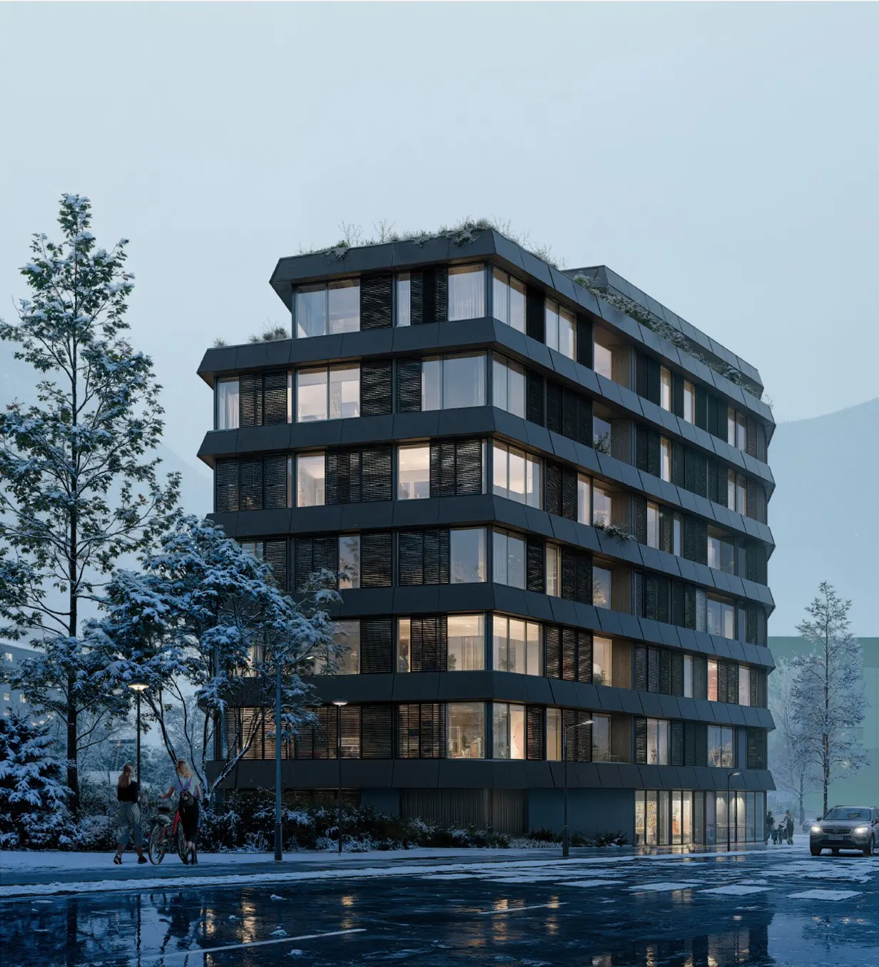Modern dark gray apartment building with large windows and green roof in winter. Snow on trees and street.