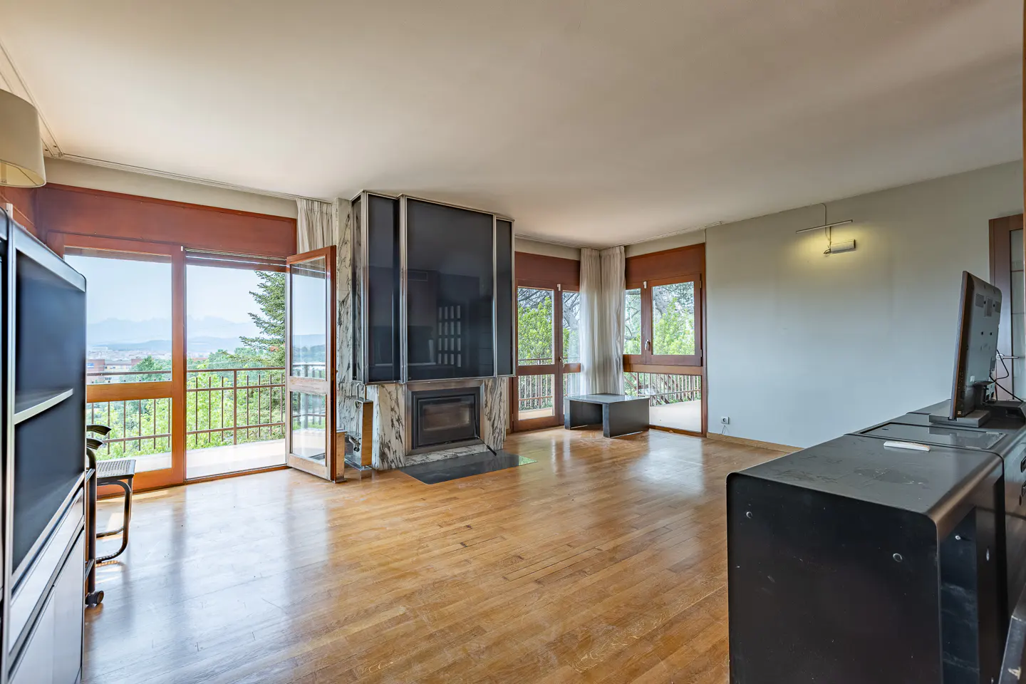 Spacious living room with hardwood floors, a central marble fireplace, and large glass doors opening to a balcony view.