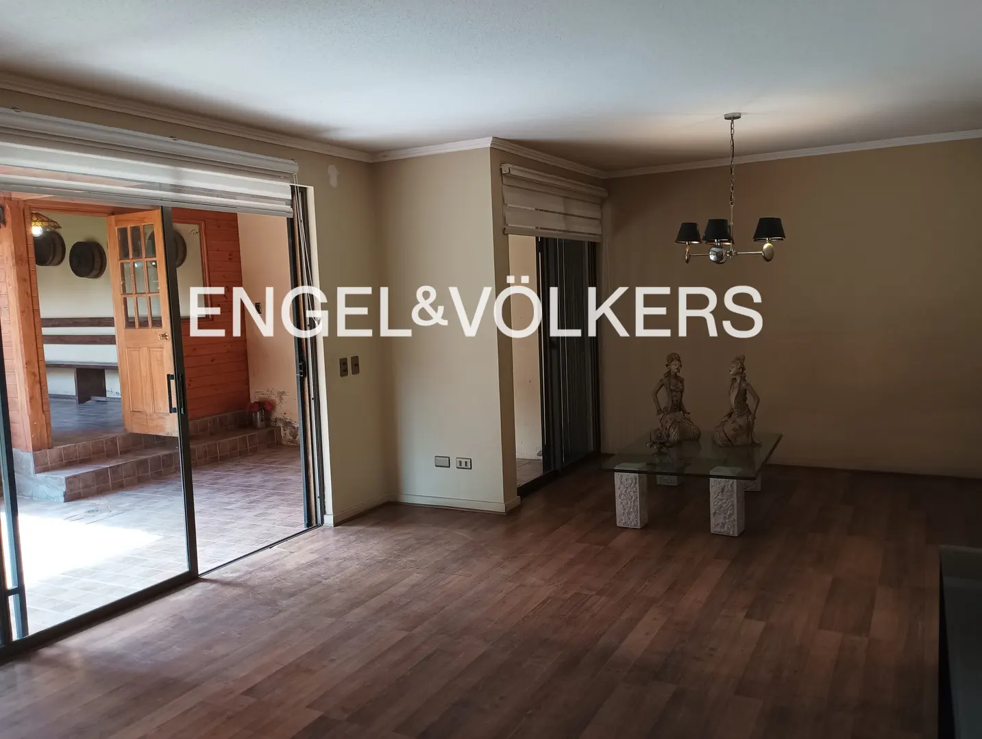 A living room with wood floors, beige walls, and a glass coffee table with two statues. Sliding glass doors lead to a patio.