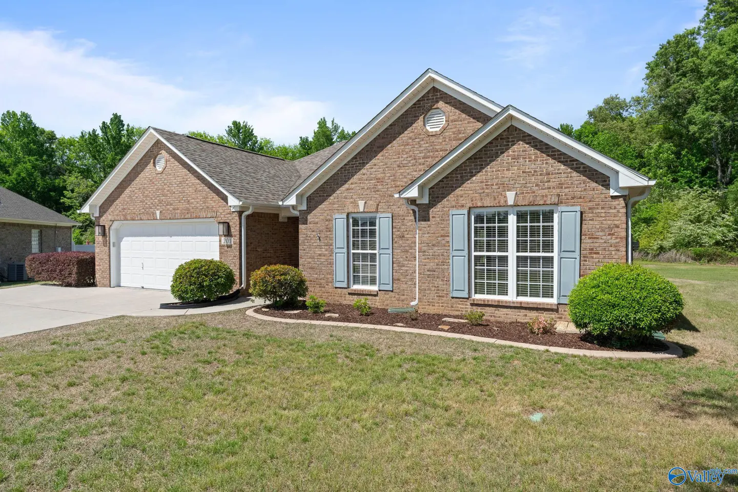 A single-story brick house with light blue shutters and a white garage door on a sunny day.