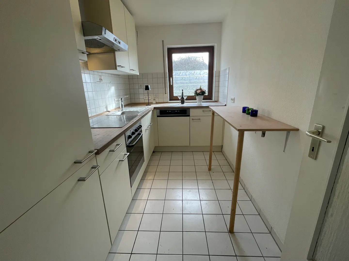 A bright kitchen with white cabinets, a sink, an oven, and a small wooden table. A window is above the sink.