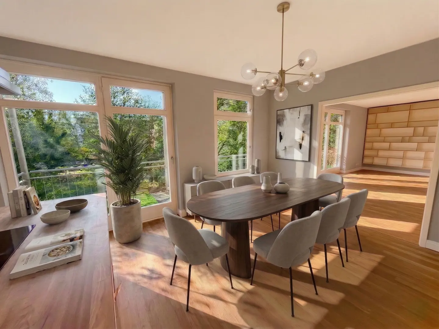 A dining room with a dark wood table, light gray chairs, and a modern chandelier. Large windows offer a view of greenery.