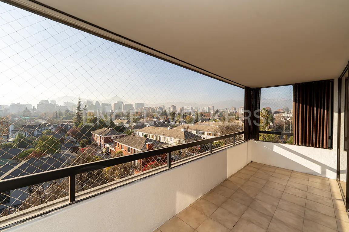 Balcony view with black railing and safety net overlooking a city with buildings and mountains in the background.