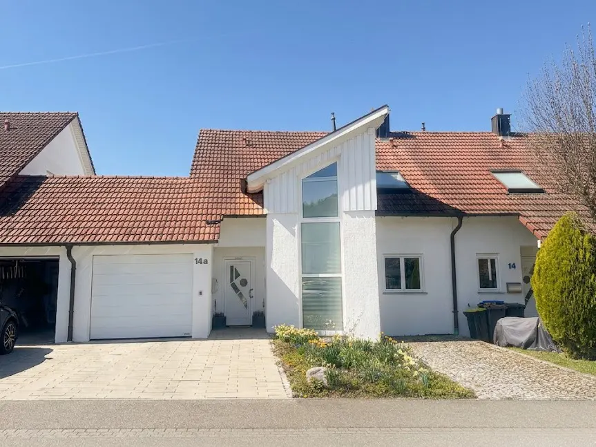 A white, modern-style house with a red tile roof under a clear blue sky. A garage is attached to the left side of the house.