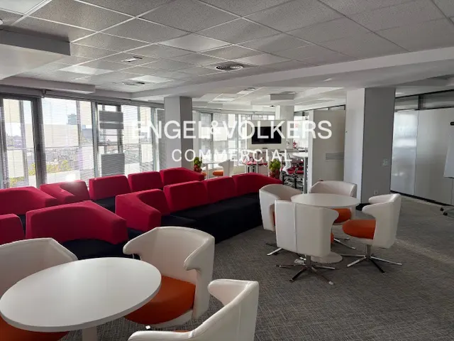 Engel & Volkers commercial space with red and black sofa, white tables and orange and white chairs.