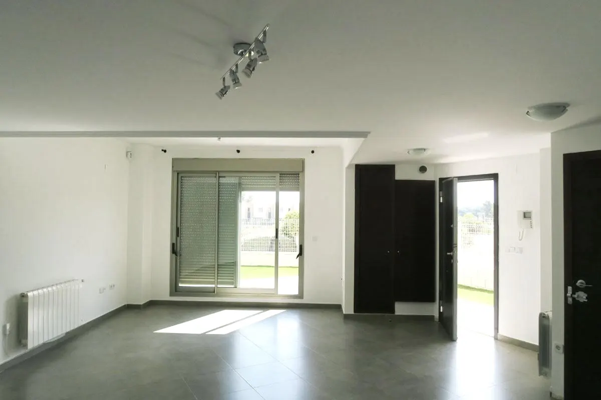 Bright, empty room with white walls, gray tile floor, and black closet. Sliding glass door leads to a green lawn. Silver light fixture on the ceiling.
