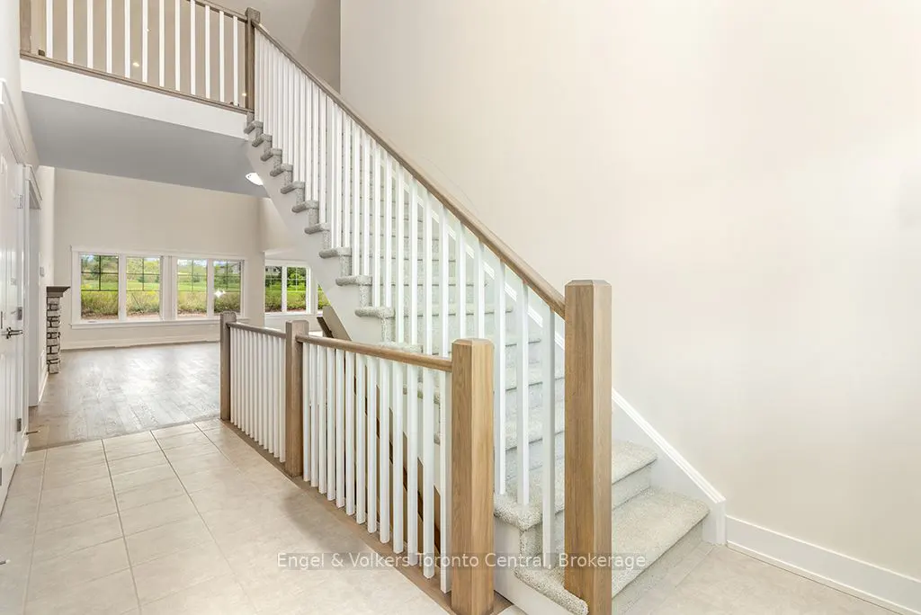 Bright foyer with tiled floor, white walls, and carpeted stairs with white and wood railing leading to a second floor. Living room visible.