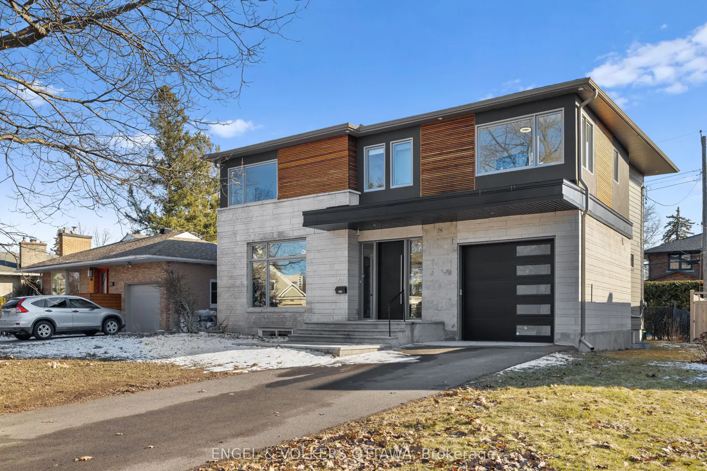 Two-story modern home with stone and wood facade, black trim, and a black garage door. A driveway leads to the house.