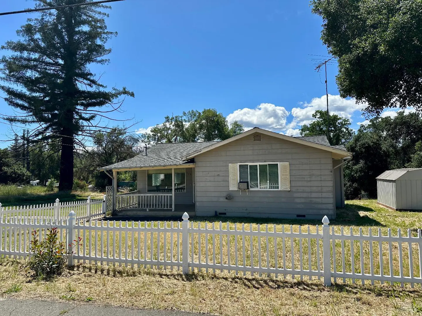 A single-story gray house with a white picket fence on a sunny day.
